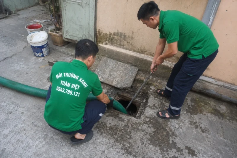 Hai nhân viên đưa ống vào ô mở trên nền sân