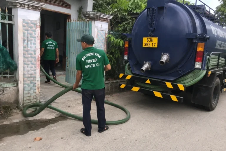Nhân viên kéo ống mềm từ xe bồn qua cổng nhà