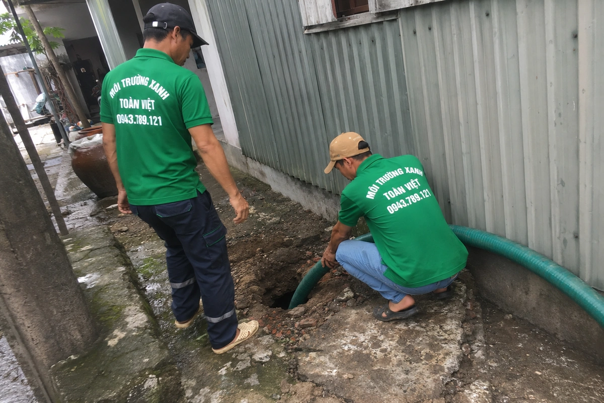 Hai nhân viên đưa ống hút xuống hầm tự hoại ở lối đi bên hông nhà