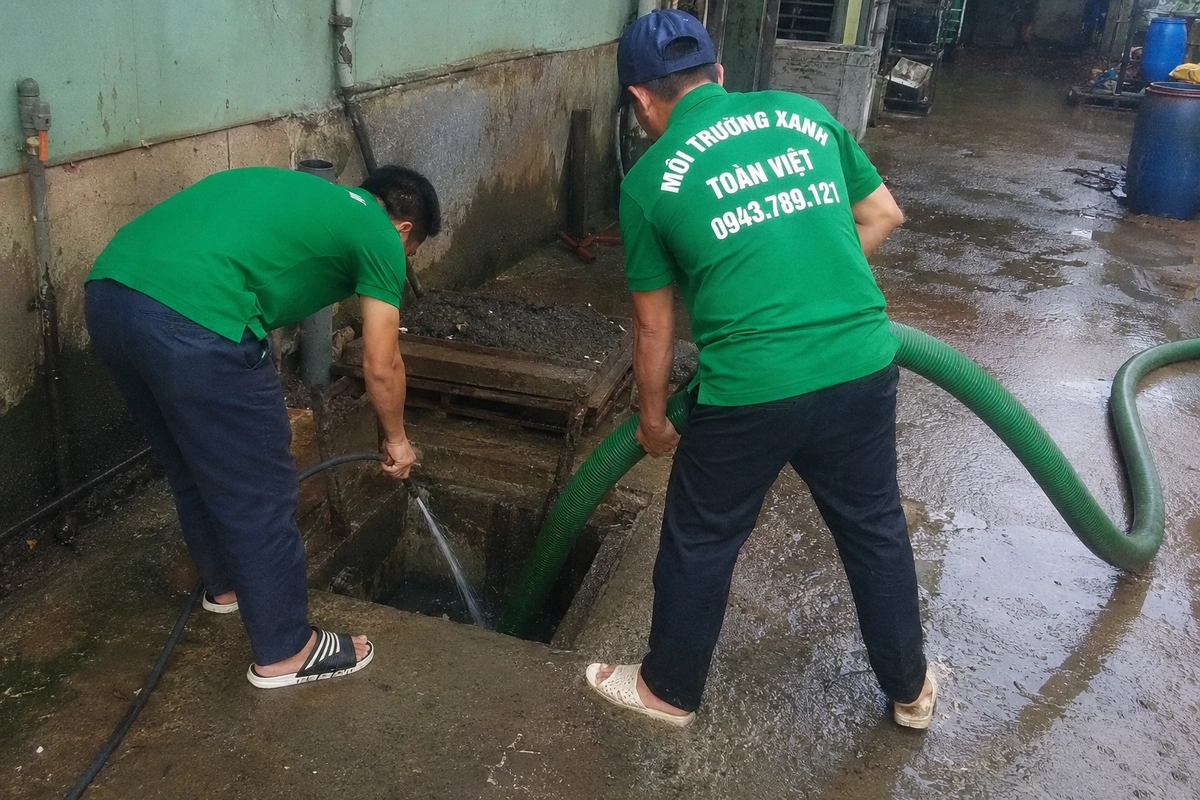 Hai nhân viên đưa ống hút xuống hầm chứa tại khu vực sân của nhà xưởng