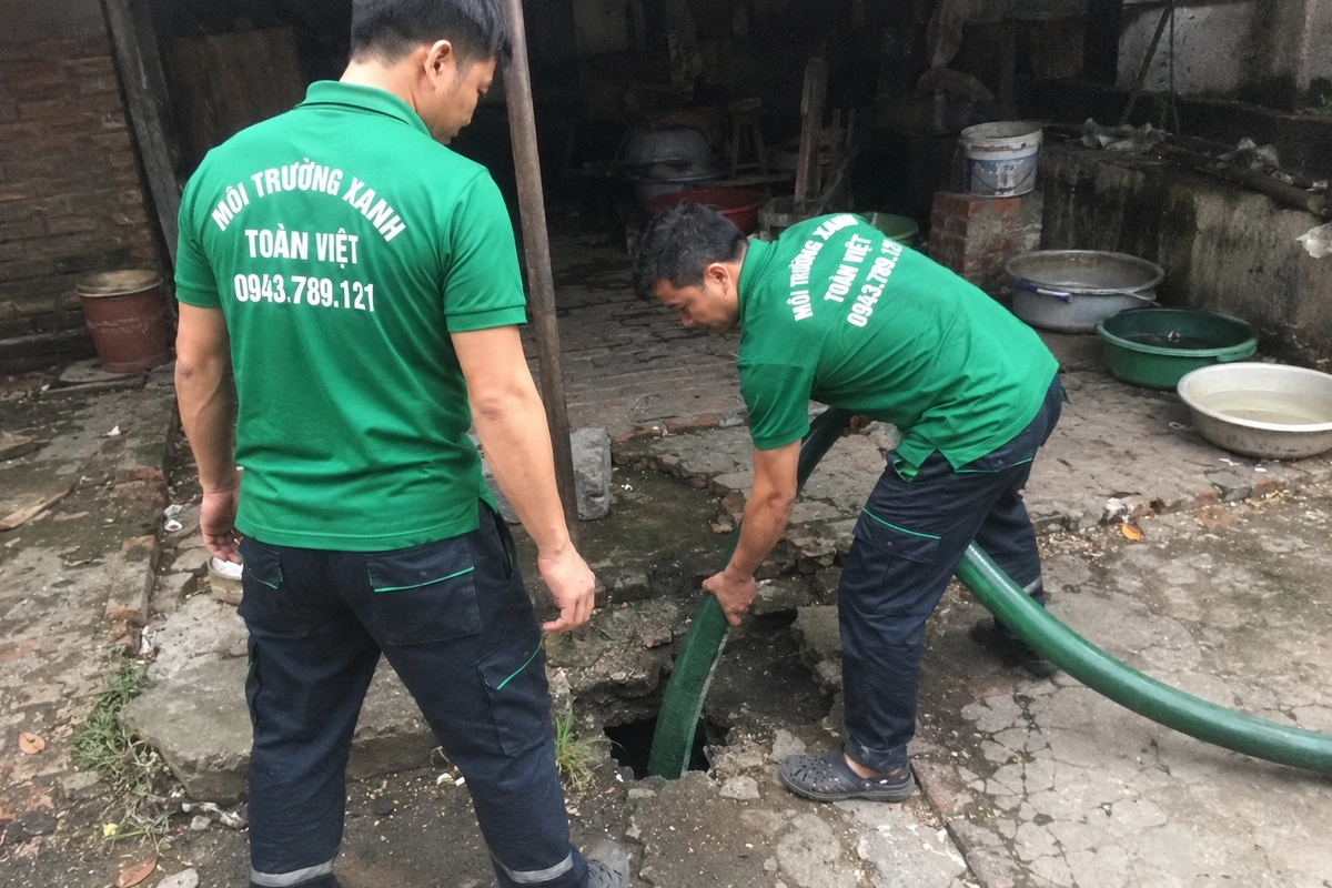 Hai nhân viên đưa ống hút xuống hầm tự hoại ở sân sau cơ sở kinh doanh