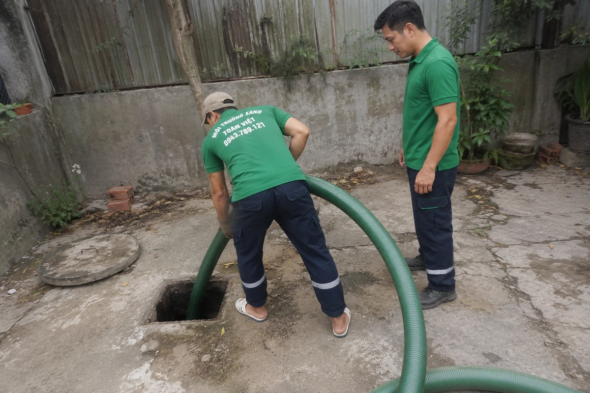 Nhân viên mở nắp hầm tự hoại và đưa ống hút xuống kiểm tra hiện trạng