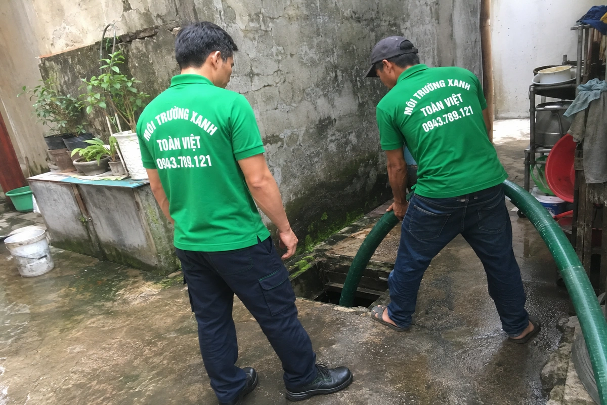 Nhân viên mở nắp hầm ngoài sân và đưa ống hút xuống hầm tự hoại