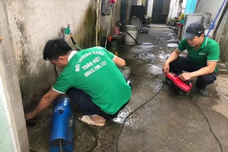 Hai nhân viên phối hợp máy và dây thông ở lối đi ngoài nhà