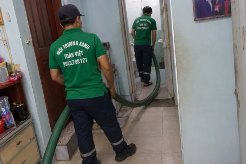 Hút hầm cầu Chợ Gạo giá rẻ uy tín | Toàn Việt 11 Hai nhân viên kéo ống hút qua hành lang trong nhà