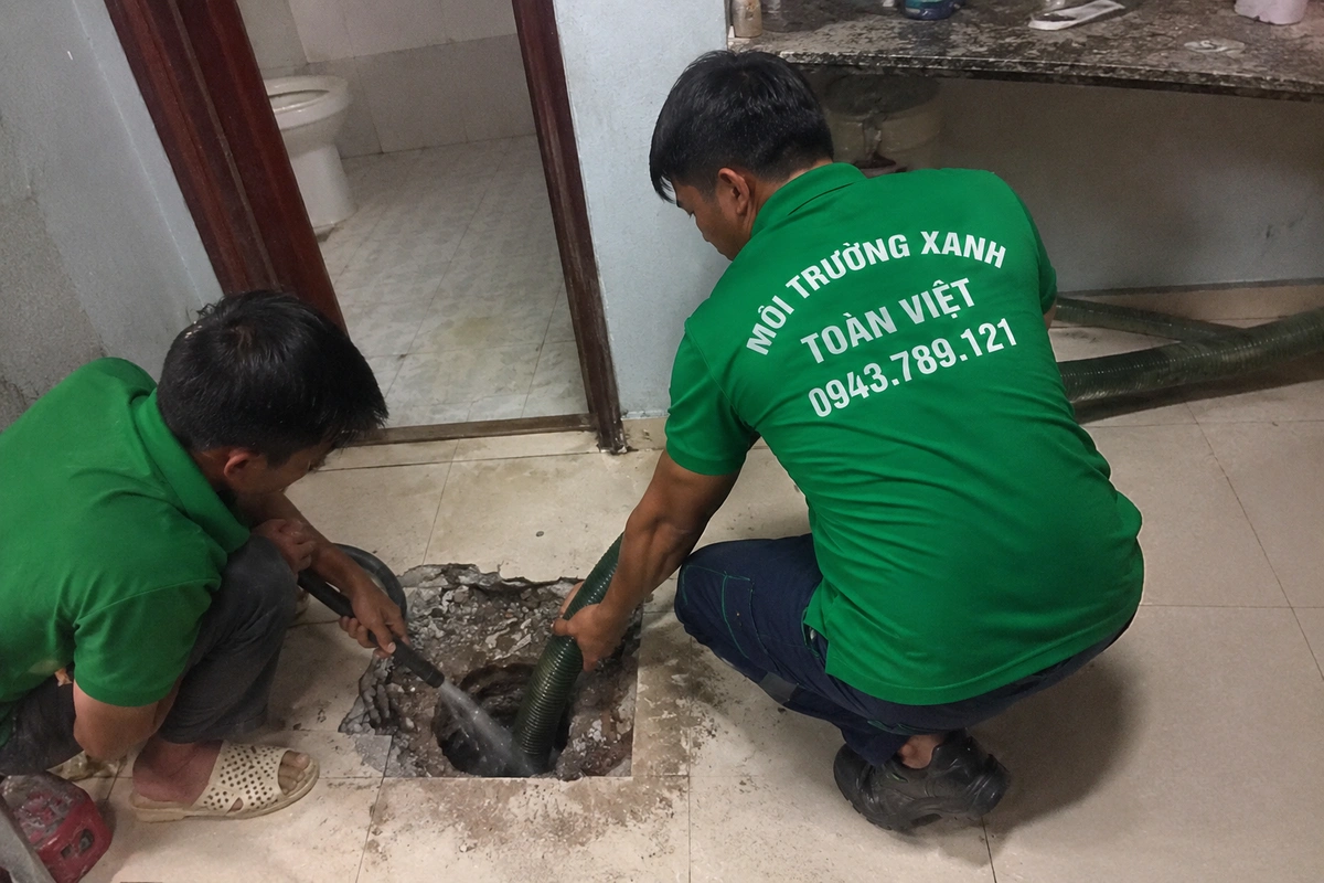 Hai nhân viên hút hầm cầu tại nắp hầm trong nhà