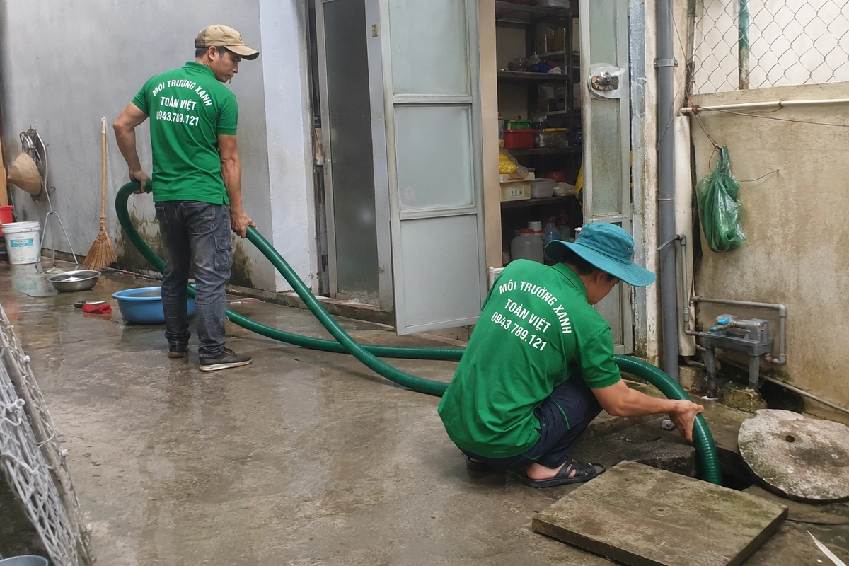 Nhân viên thao tác tại miệng hầm cầu trong khu vệ sinh