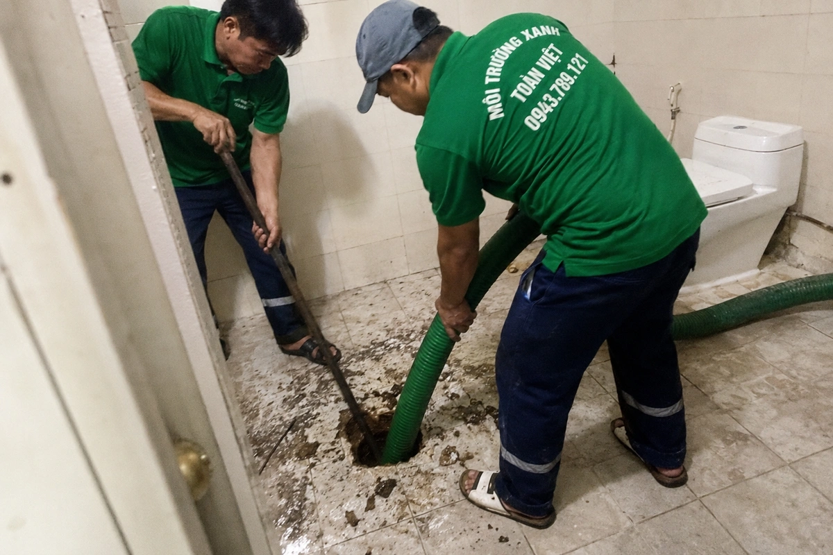 Nhân viên thao tác tại miệng hầm cầu trong khu vệ sinh