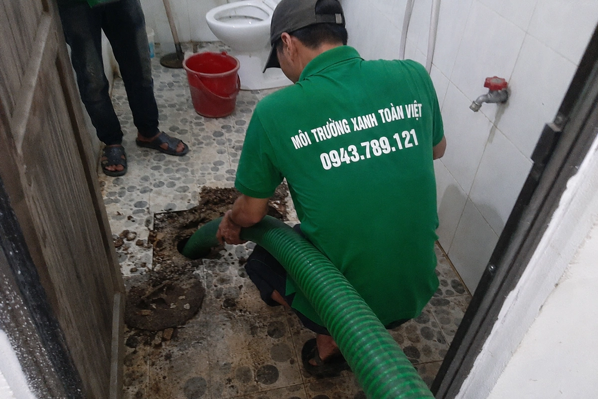 Nhân viên thao tác tại miệng hầm cầu trong khu vệ sinh