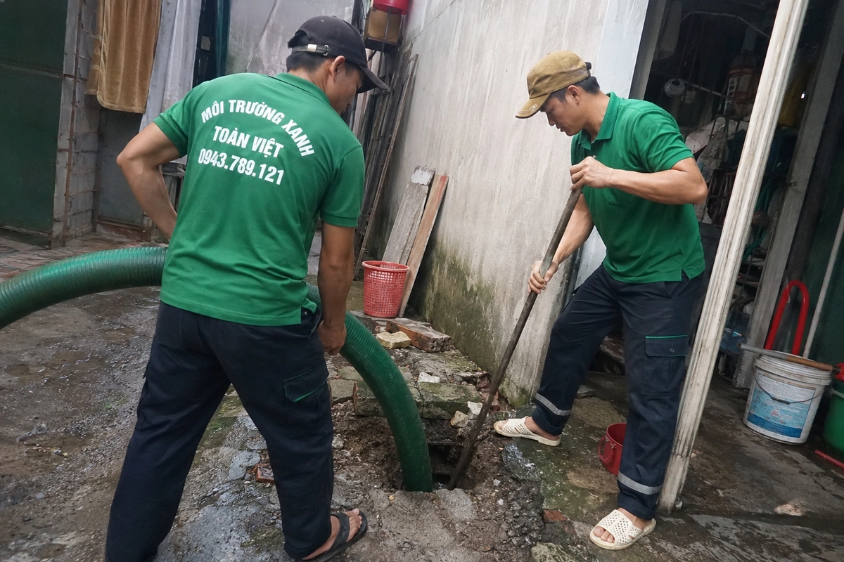 Hai nhân viên thao tác tại miệng hầm cầu đã mở nắp