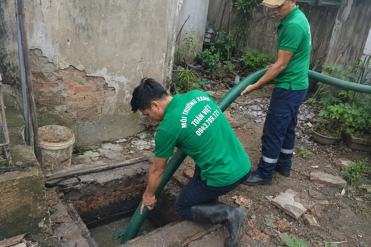Hai nhân viên thao tác tại miệng hầm cầu đã mở nắp