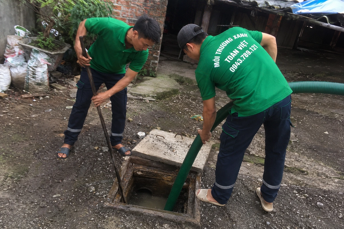 Hai nhân viên thao tác tại miệng hầm cầu đã mở nắp