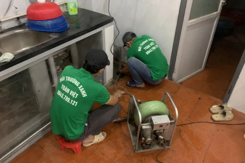 Hai nhân viên đặt máy cạnh đường thoát dưới khu rửa bếp