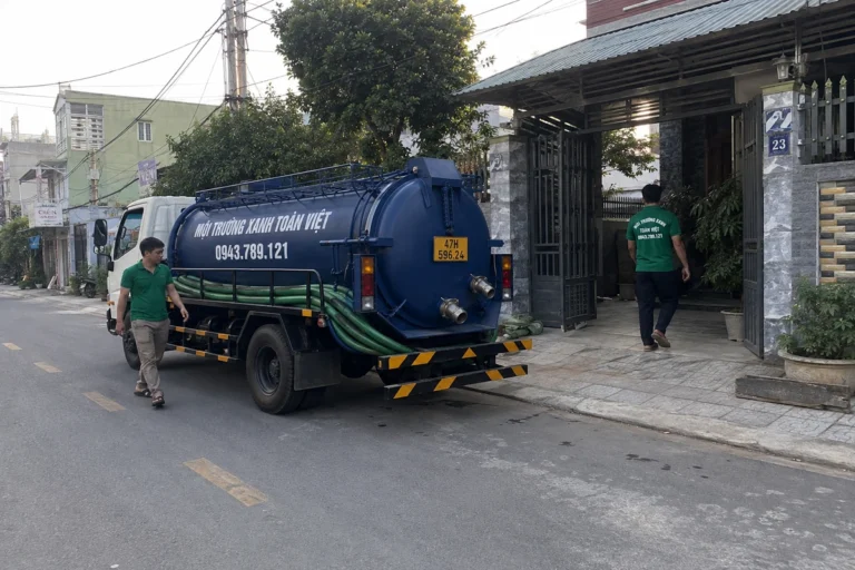 Xe bồn và nhân viên trước cổng nhà, ống nối về phía sân.