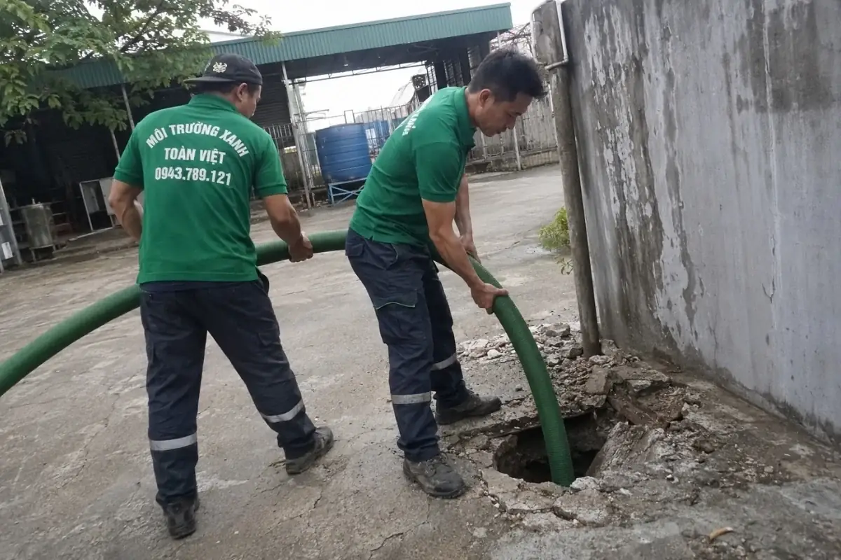 Hai nhân viên giữ ống tại miệng hầm cạnh tường
