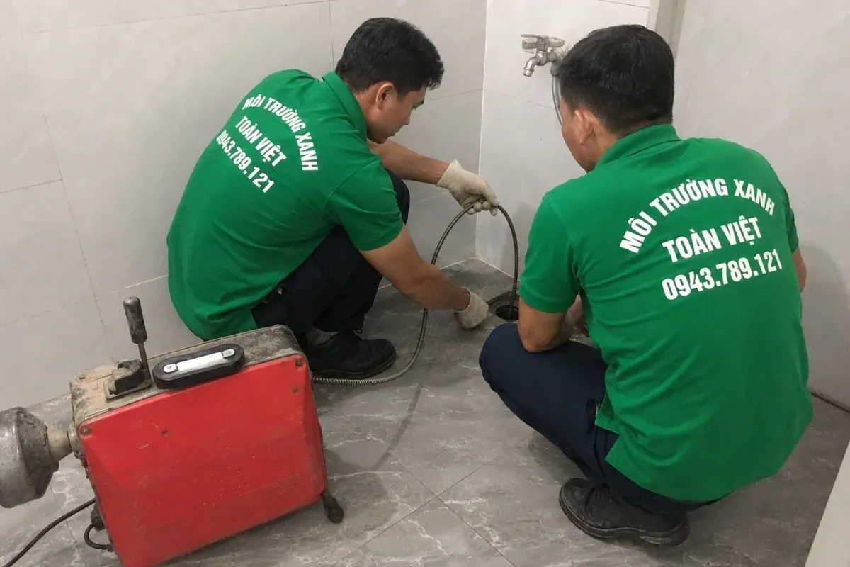 Hai nh&acirc;n vi&ecirc;n phối hợp c&ugrave;ng d&acirc;y l&ograve; xo tại miệng tho&aacute;t s&agrave;n dưới v&ograve;i nước