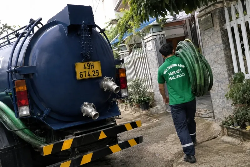 Nh&acirc;n vi&ecirc;n k&eacute;o ống b&ecirc;n cạnh xe bồn m&agrave;u xanh