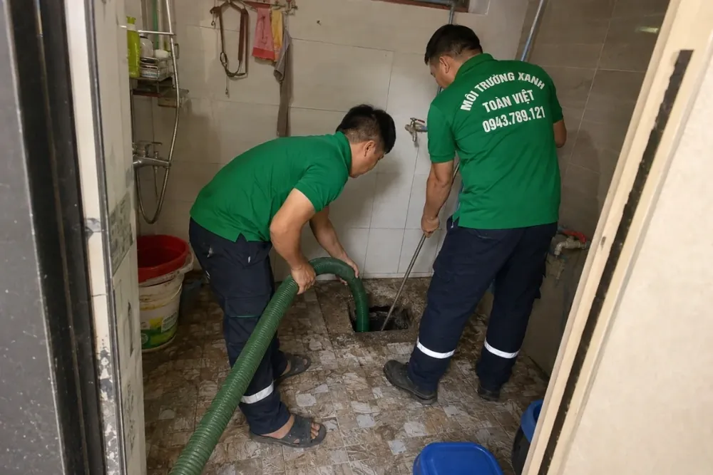 Hút hầm cầu Tân Bình giá rẻ uy tín | Toàn Việt 8 Hai nhân viên và ống hút tại điểm mở trên nền bên trong nhà
