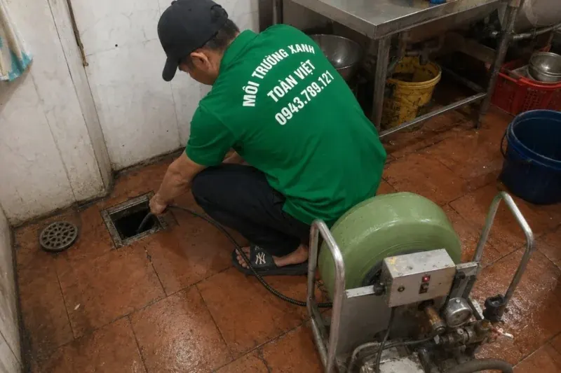 Nh&acirc;n vi&ecirc;n đưa d&acirc;y m&aacute;y l&ograve; xo m&agrave;u xanh qua cửa thăm khu bếp &ndash; th&ocirc;ng cống nghẹt Củ Chi