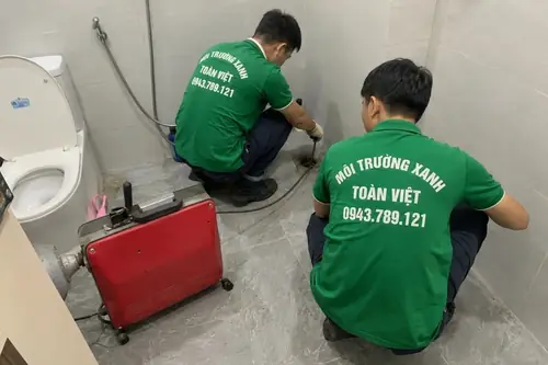 Hai nhân viên phối hợp dây máy trong phòng vệ sinh.