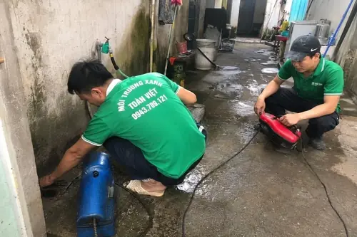 Hai nhân viên thao tác với máy và dây ở lối ngoài nhà.