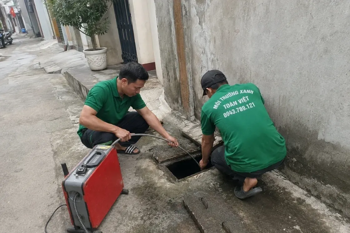 Hai nhân viên làm việc bên hố ga và thiết bị thông cống