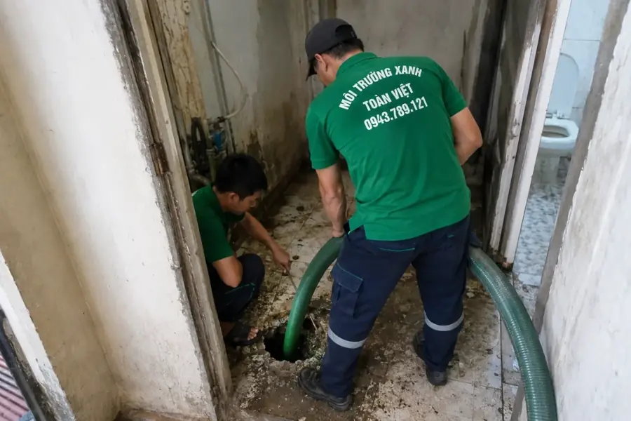 Hút hầm cầu Bình Thạnh giá rẻ uy tín | Toàn Việt 13 Hai nhân viên đưa ống hút vào điểm mở trên nền cạnh khu vệ sinh.