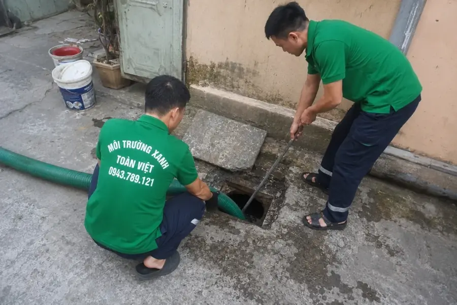 Hai nhân viên Toàn Việt thao tác tại ô mở cạnh tường, nắp bê tông được đặt bên cạnh.